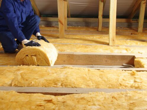 Construction worker thermally insulating house attic with fiberglass