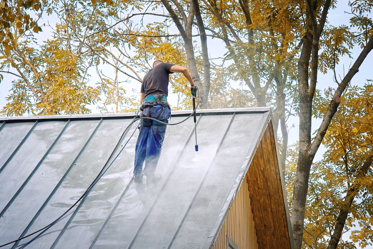 an with pressure washer gun washing roof of private house. 