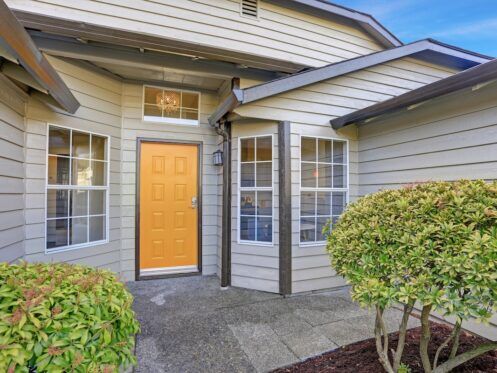 Entrance porch with taupe exterior paint, yellow front door and large windows.