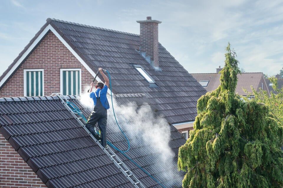 black streaks on roof-roofer standing on roof ladder while power washing roof of brick house