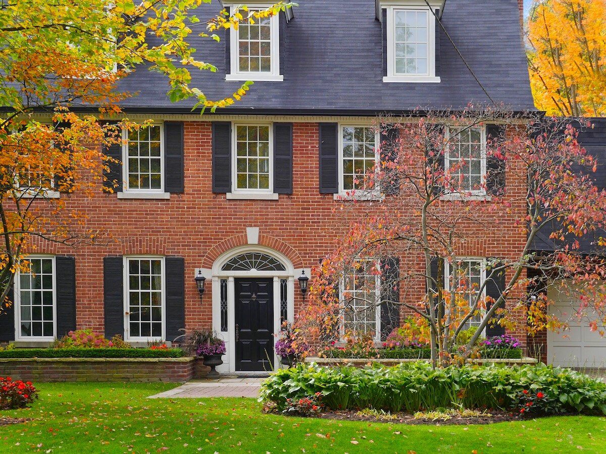 large suburban brick house in fall, pretty landscaping frames the front of the house