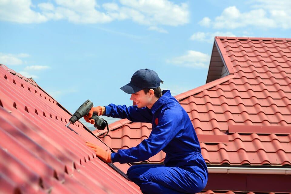 how to install metal roofing over shingles-roofer in blue working suit installing red metal roof on a house
