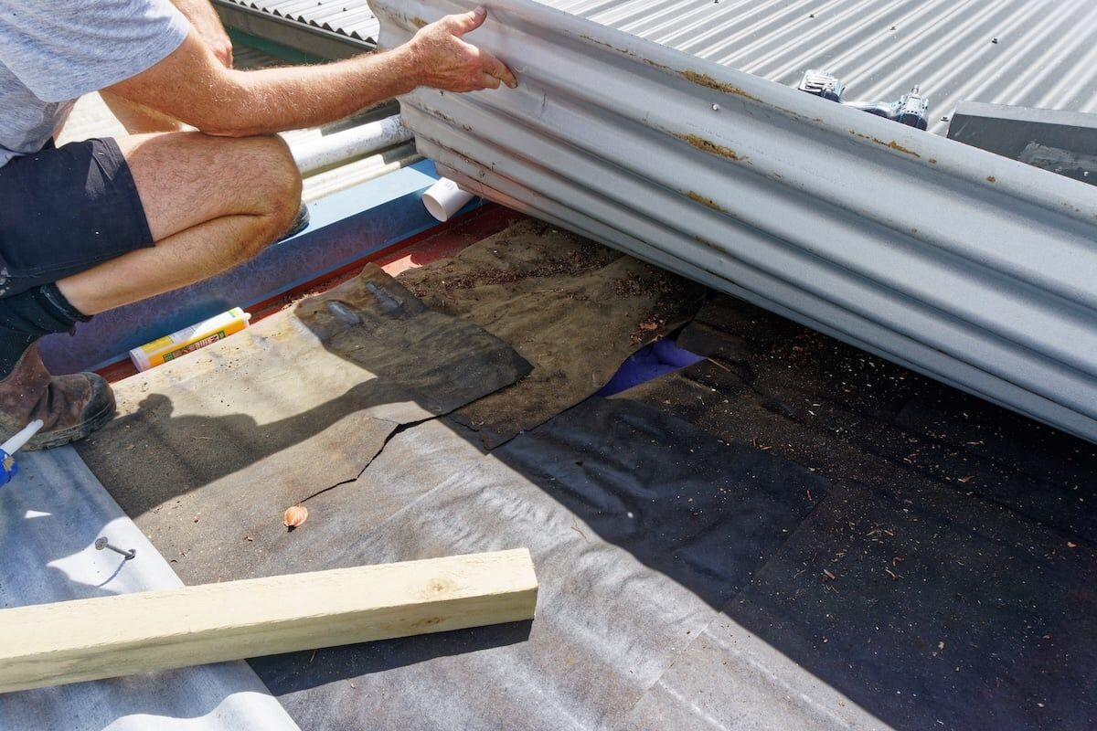 Builder looking under a corrugated iron roof for a water leak.