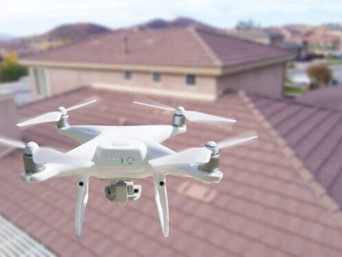 Unmanned Aircraft System (UAV) Quadcopter Drone In The Air Over House Inspecting the Roof.
