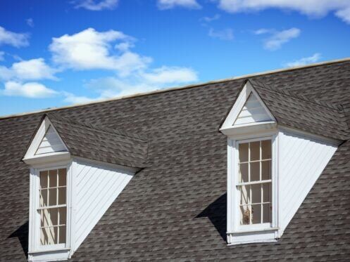 Two white wood dormers on a grey shingle roof under blue sky
