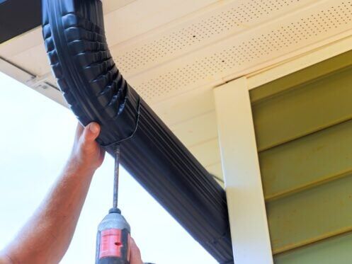 During installation of rain gutters on roofs, worker is fitting downpipe bending downspout
