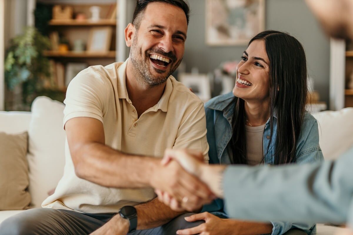 couple smiling shaking hands with man out of sight
