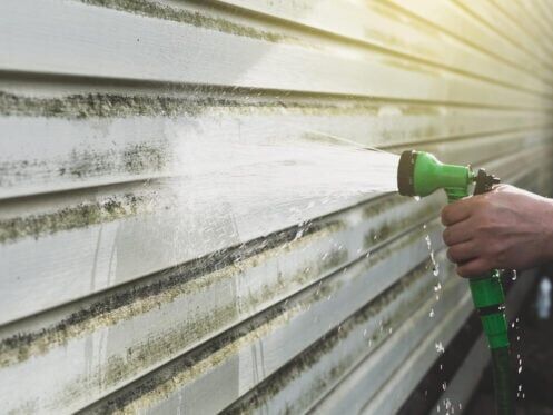 how to clean vinyl siding-person using garden hose to clean vinyl siding on house