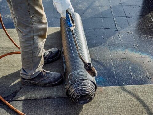 Roof waterproofing with bituminous membrane being installed.