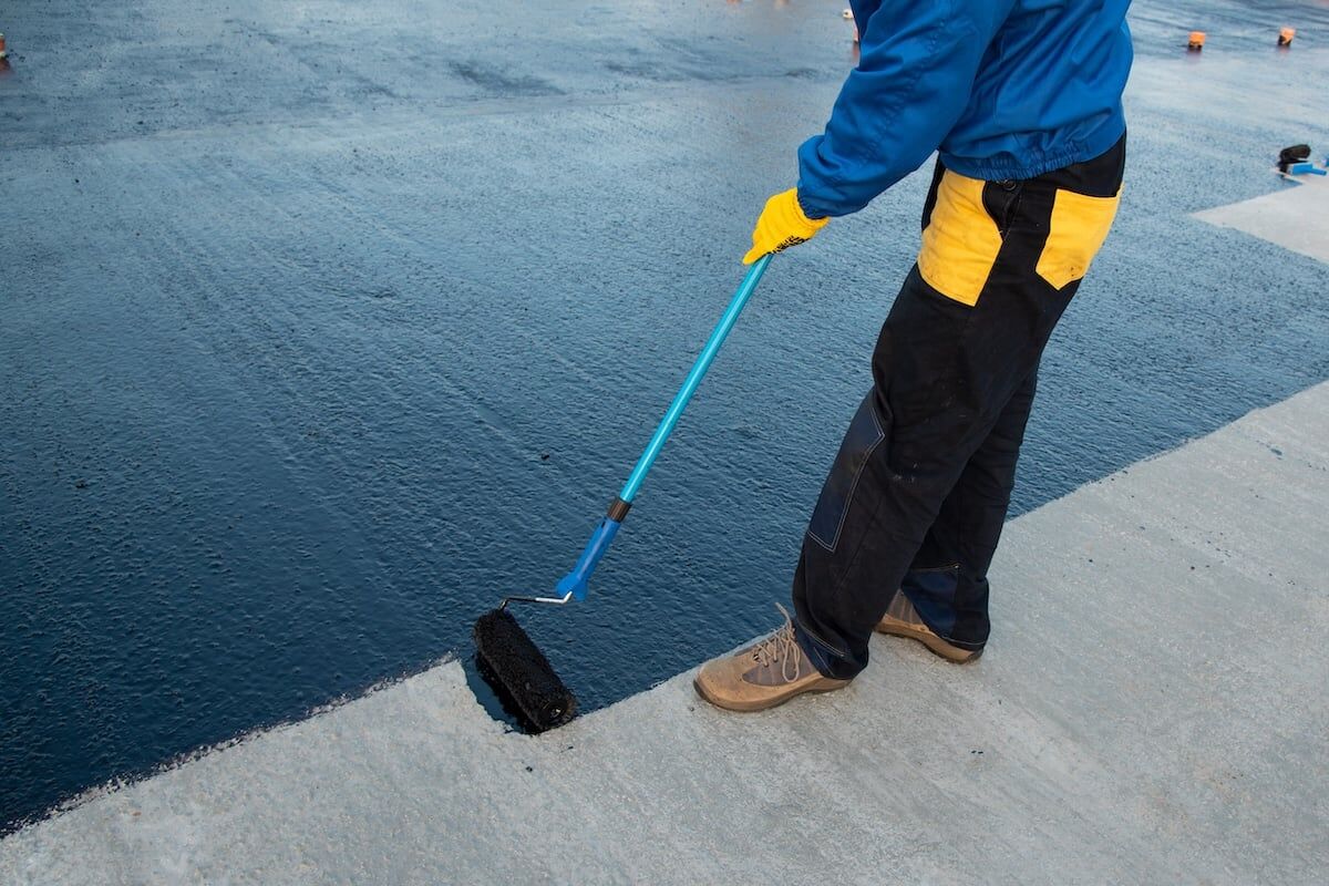 Waterproofing coating. Worker applies bitumen mastic on the foundation. Roofer cover the rooftop polymer modified bitumen waterproofing primer, with a roller brush.