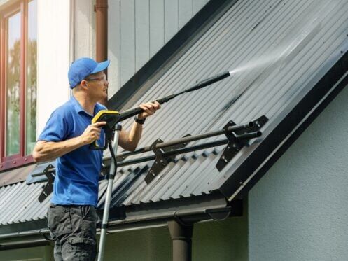 man standing on ladder and cleaning house metal roof with high pressure washer