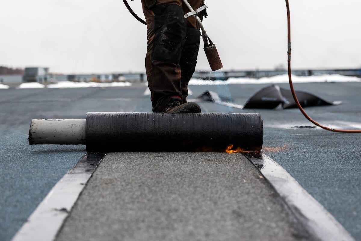 professional roofer securing rolled tar with a blowtorch on a flat roof installation process