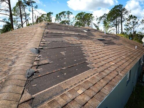 Damaged house roof with missing shingles after storm