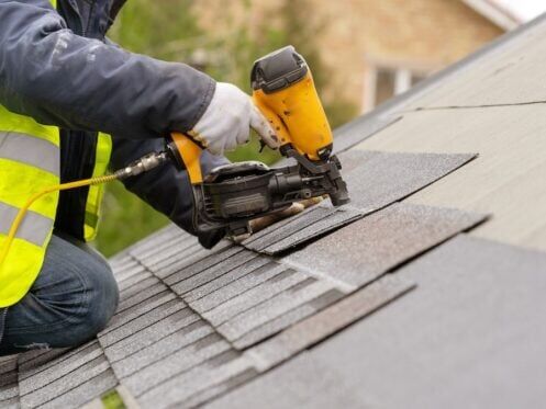 Roofer uses a nail gun to install shingles on roof