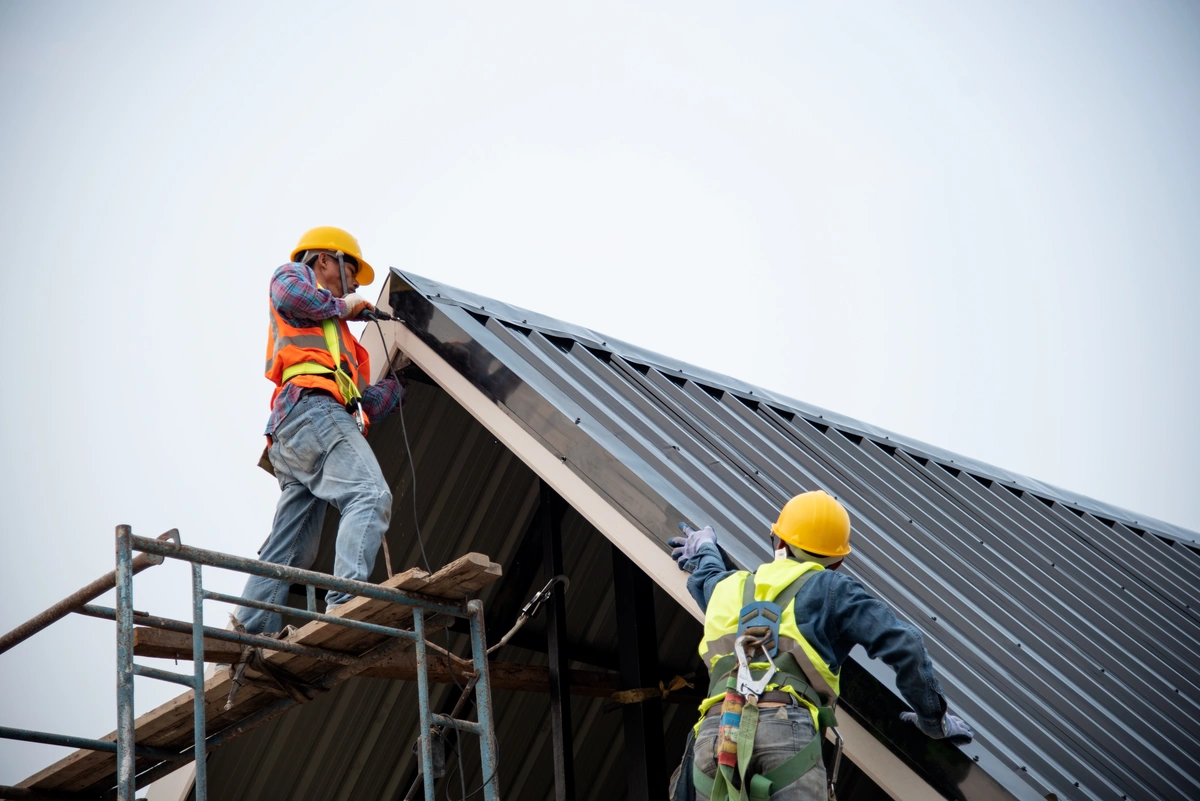two men in harnesses installing metal roof on home