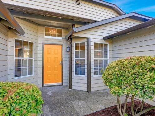 Entrance porch with taupe exterior paint, yellow front door and large windows.